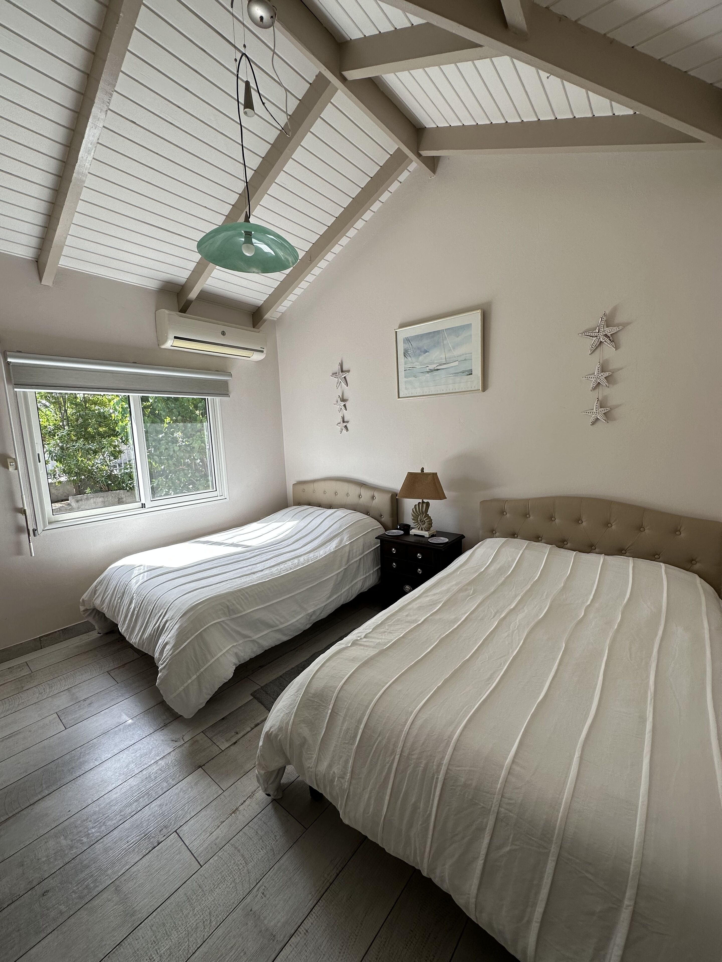 A bedroom with two beds, a window, a ceiling fan, and a painting.