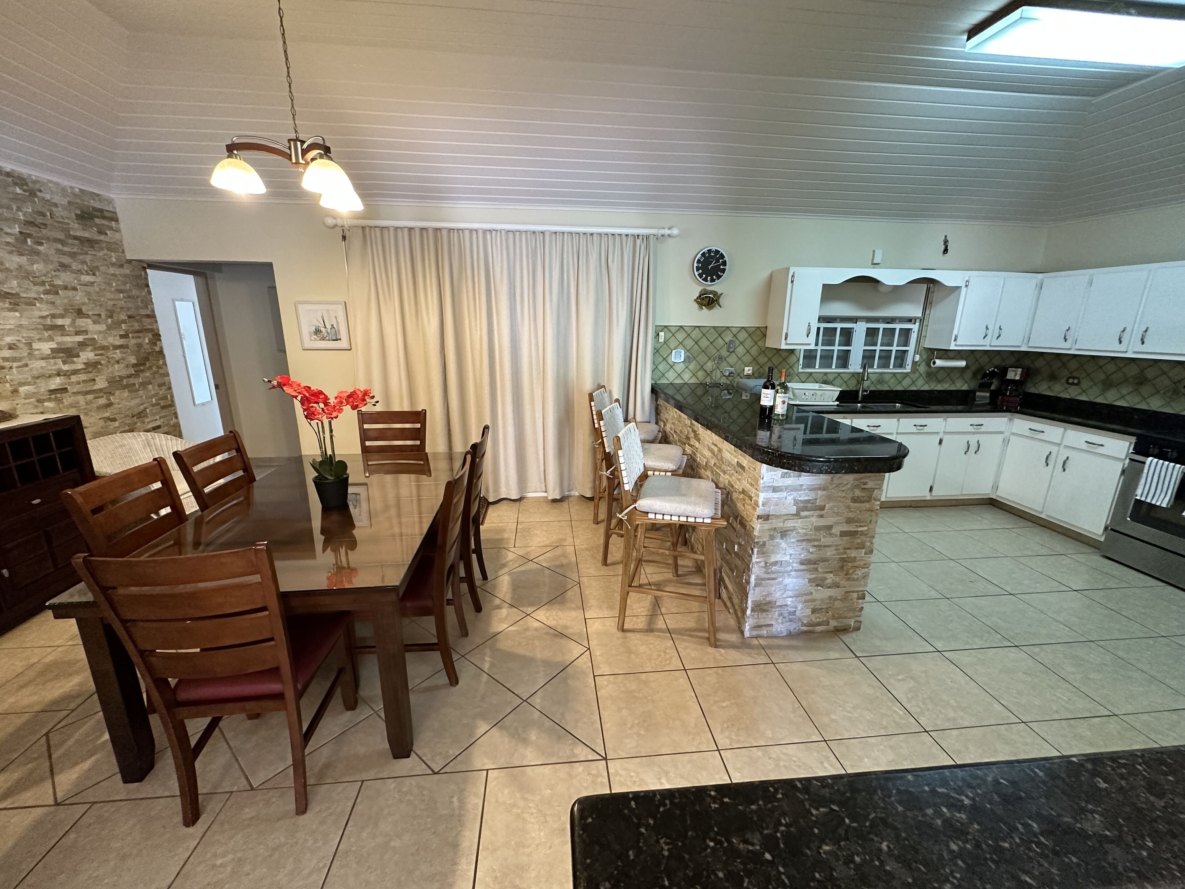 A modern kitchen with a dining area, featuring a granite countertop, wooden chairs, and a stone island.