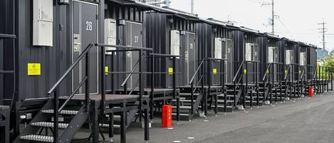 Une rangée de bâtiments modulaires noirs, numérotés de 26 à 28, dotés de boîtiers électriques et d’escaliers à l’extérieur.