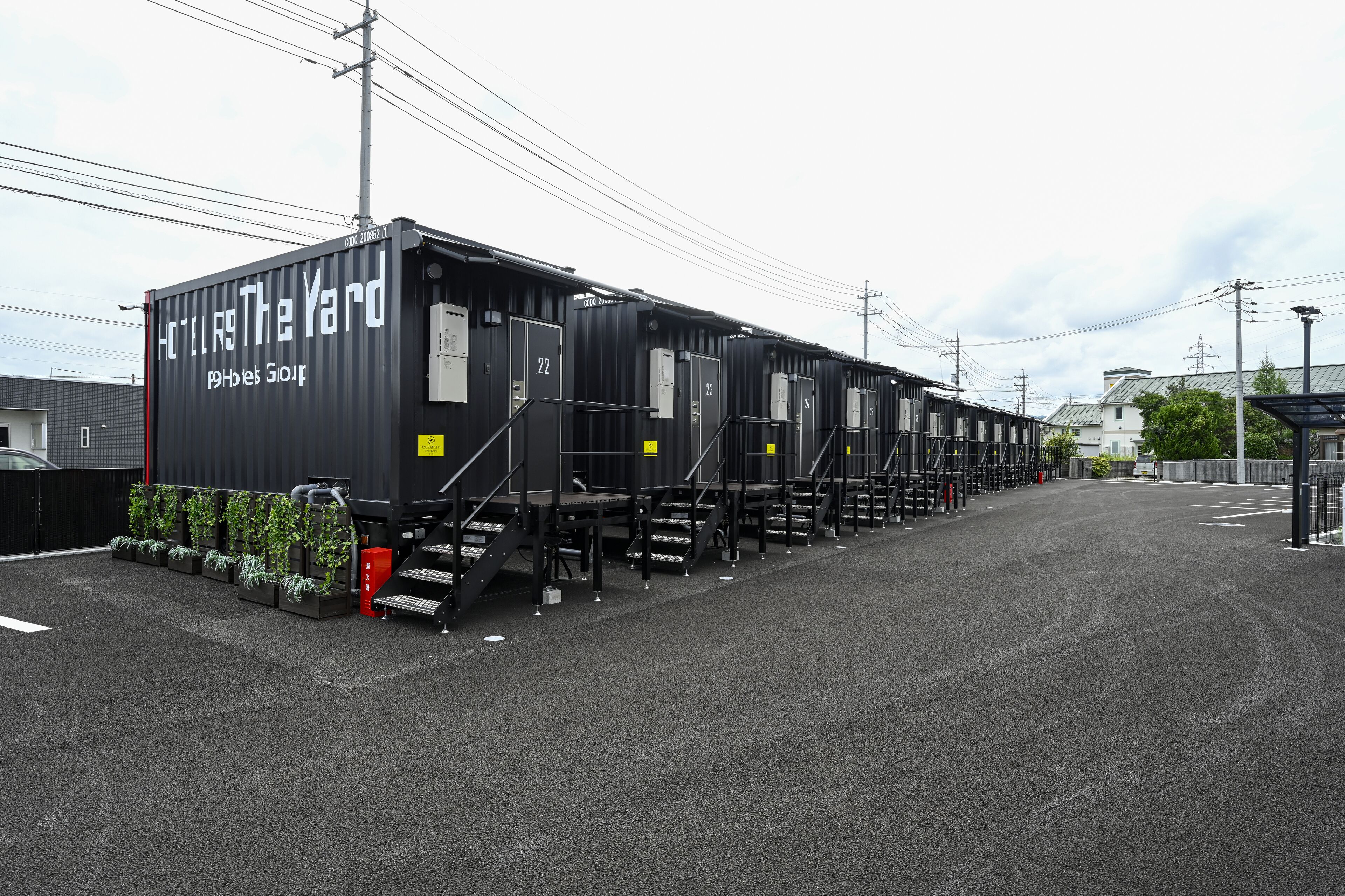 A row of black modular hotel units labeled "Hotel The Yard" with a row of green plants in front.