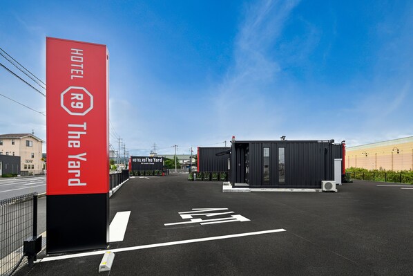 L’entrée d’un hôtel, avec une enseigne rouge bien visible, un bâtiment noir et un ciel dégagé.