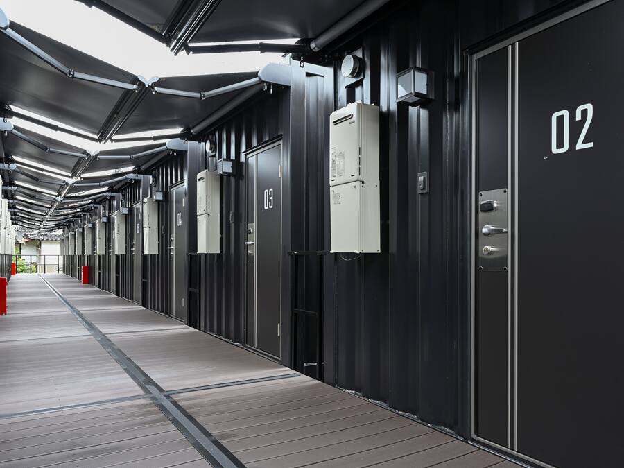Un couloir bordé de portes numérotées, qui semblent indiquer des chambres d’hôtel, et un passage.