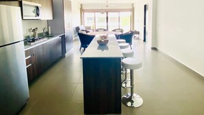 A modern kitchen with a central island, dark cabinets, and a large window providing natural light. - Brand new. Lovely 3 bedroom condo with pool Walking distance to the beach (Nuevo Vallarta)