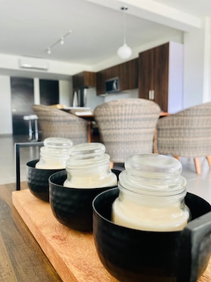 A modern kitchen with a wooden dining table, black bowls with jars, and a sofa in the background.