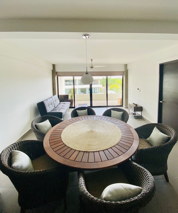 A dining area with a round table surrounded by wicker chairs, a sofa, and a ceiling fan.