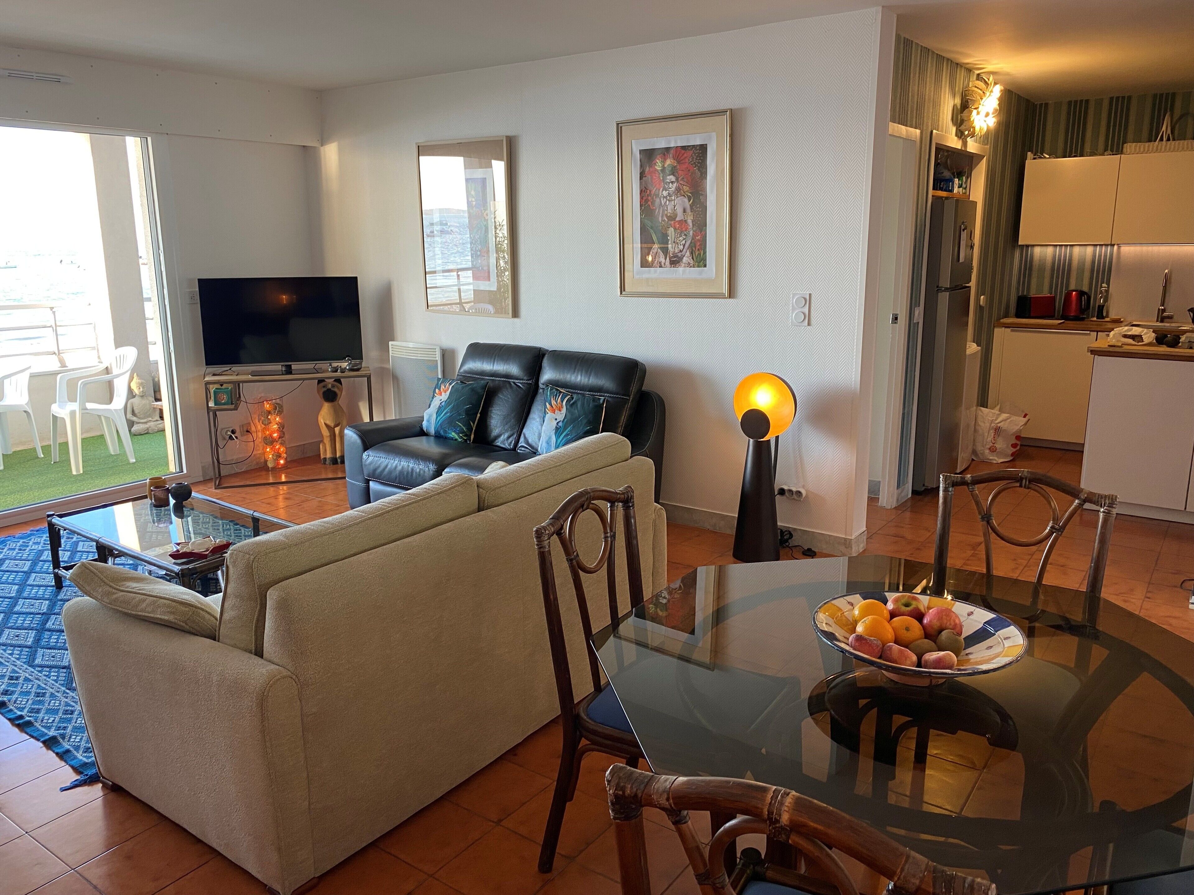 Een woonkamer met een bank, een televisie, een eettafel met fruit en een keukenhoek.