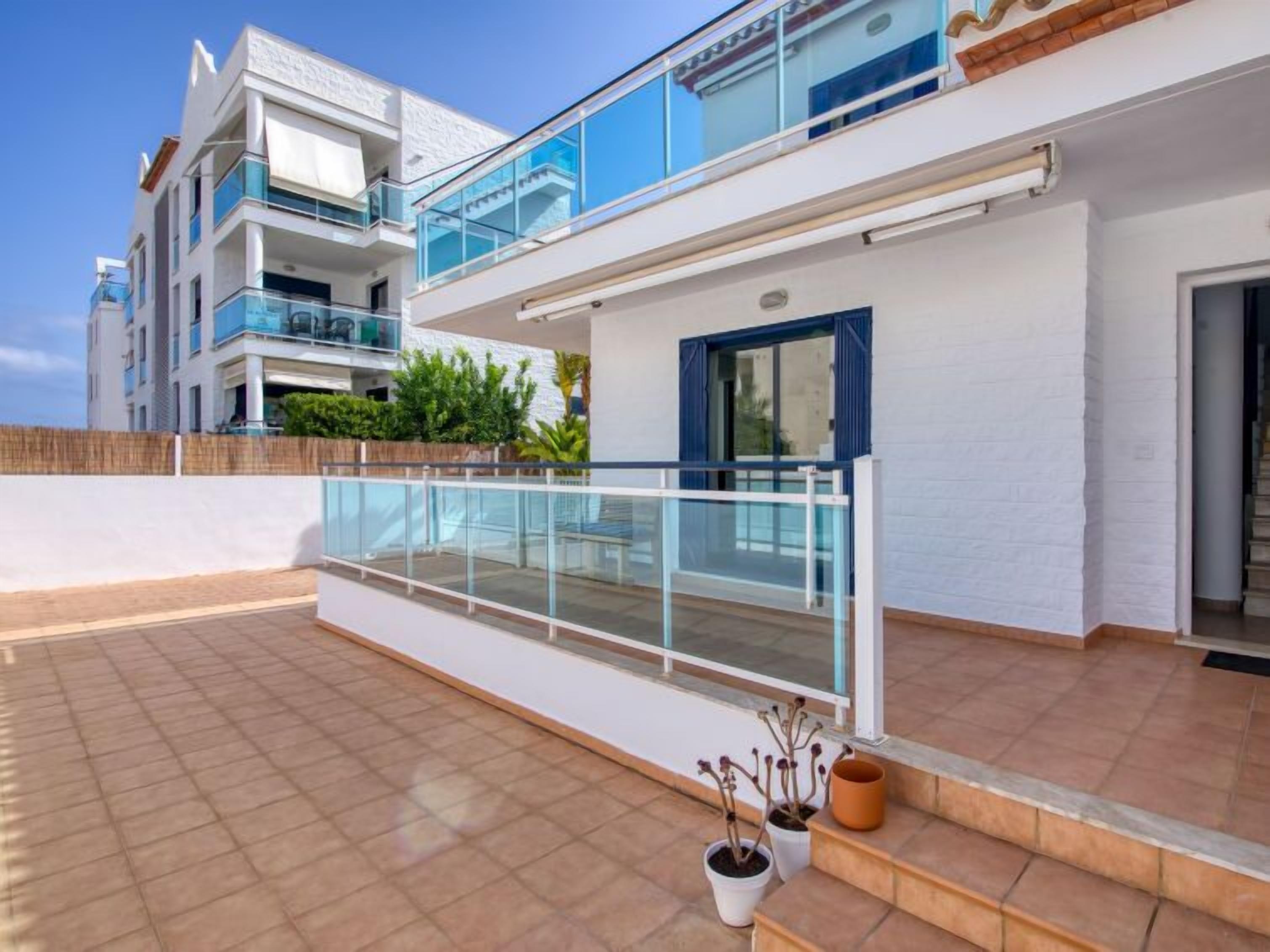Un immeuble résidentiel moderne à plusieurs étages, doté de balcons, d’une terrasse carrelée et de plantes en pot.