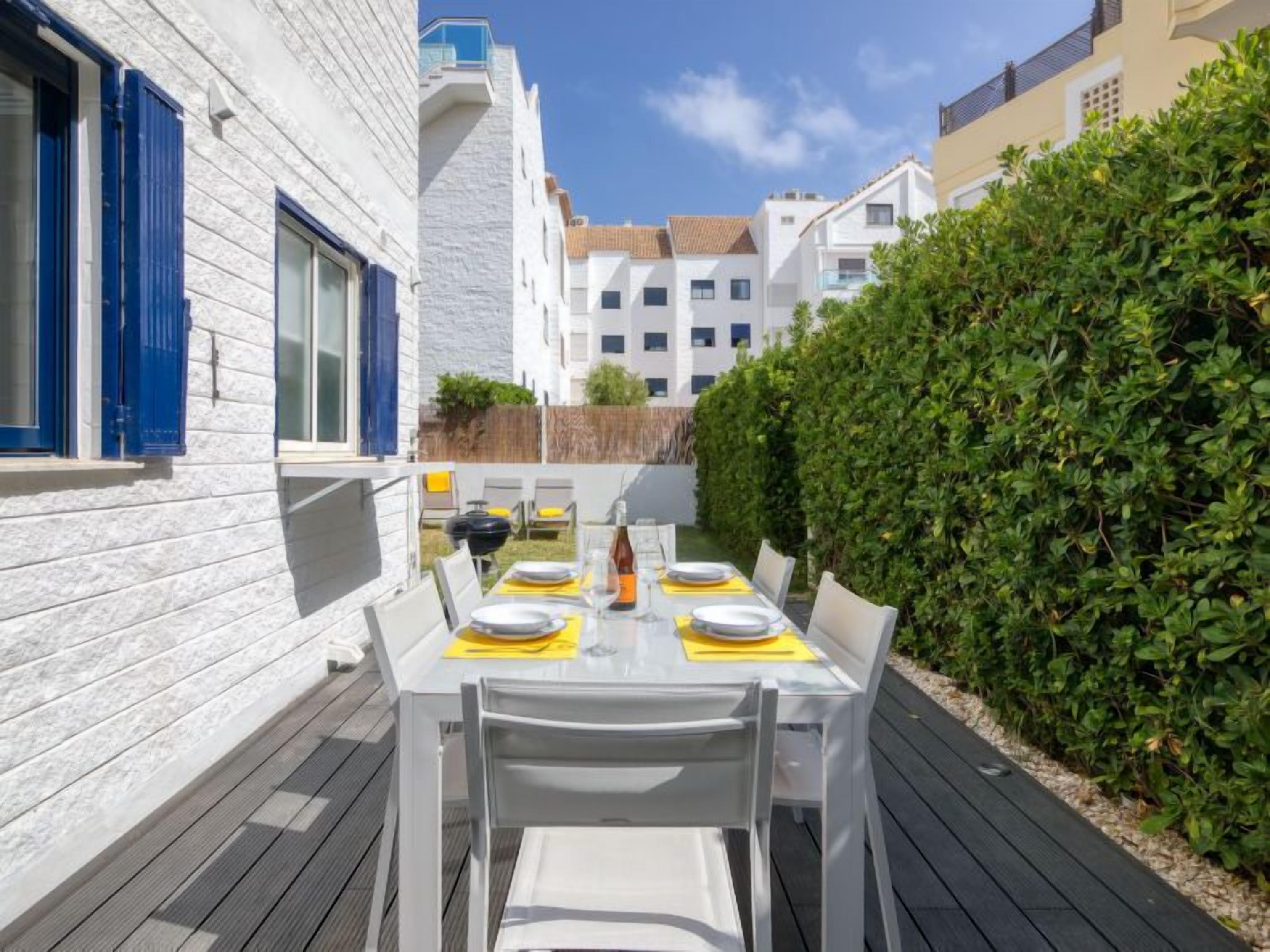 A patio with a table set for four, surrounded by white walls and a hedge.