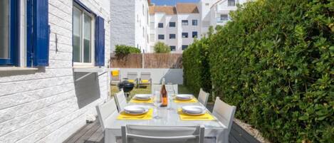 A patio with a table set for four, surrounded by white walls and a hedge.