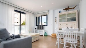 Un soggiorno moderno con un divano grigio, un tavolo da pranzo bianco con sedie, una TV e un mobile contenitore con vetrate.