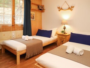 Una habitación acogedora con dos camas de madera, una mesita de noche con lámpara y una ventana con cortinas.