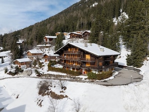 Uma grande cabana de madeira com várias varandas, cercada por árvores cobertas de neve e uma paisagem montanhosa ao fundo.