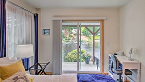 Habitación de hotel con cama, escritorio con silla, lámpara y vista a un lago con barcos.