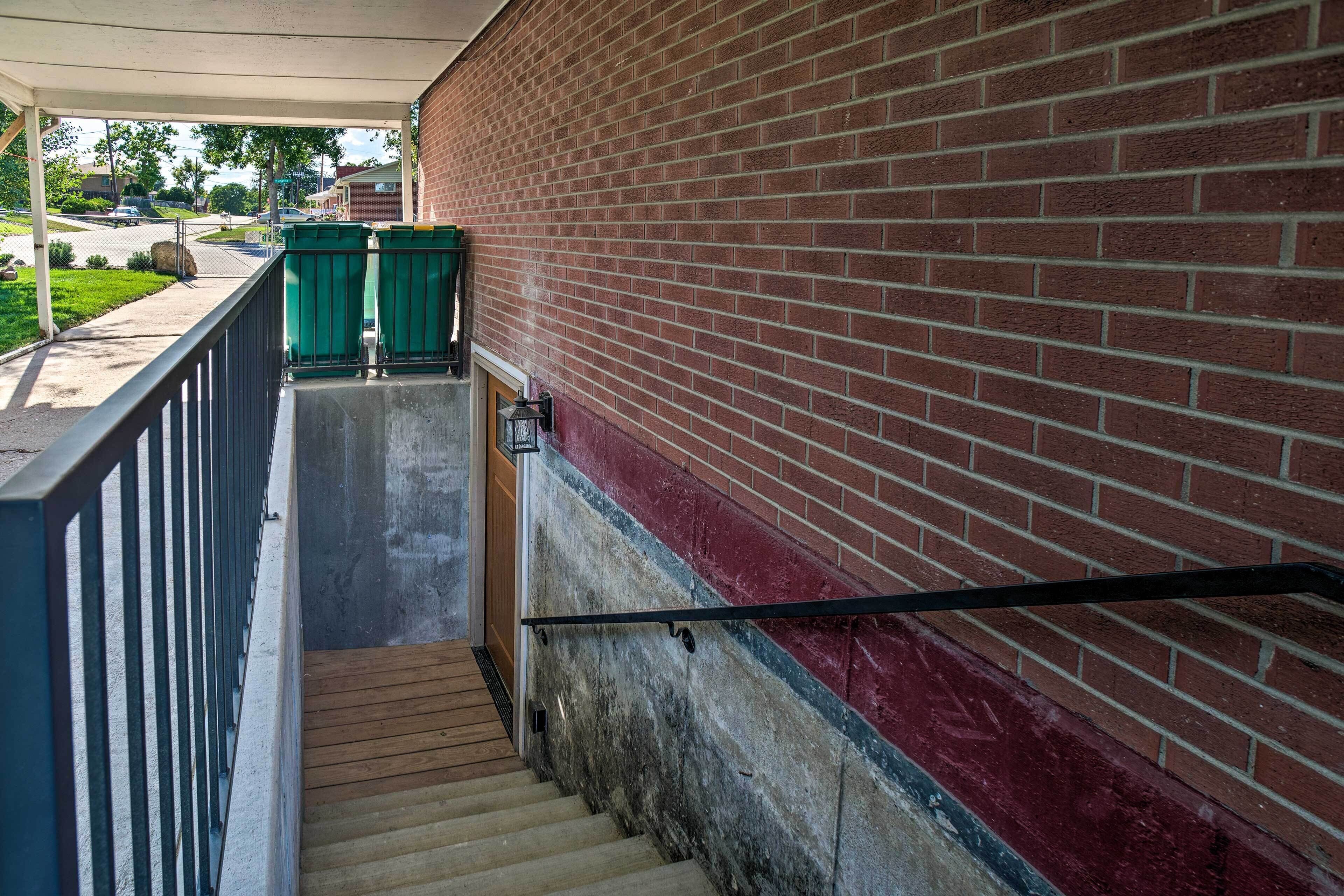 A stairway with a metal handrail, a brick wall, and a covered area with a green trash bin.