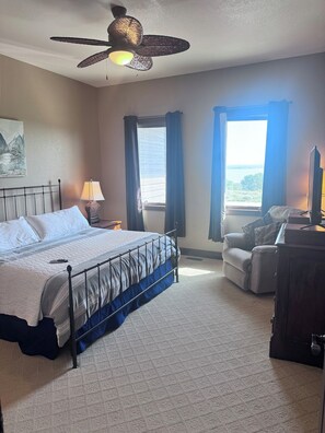 A bedroom with a bed, a desk, a chair, a ceiling fan, and a window with curtains.