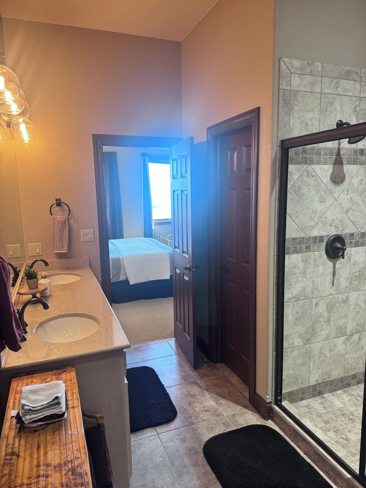 Un bagno con due lavandini, una doccia e un letto visibile attraverso una porta aperta.