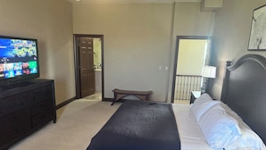 A bedroom with a bed, a dresser, a television, and a door leading to another room.
