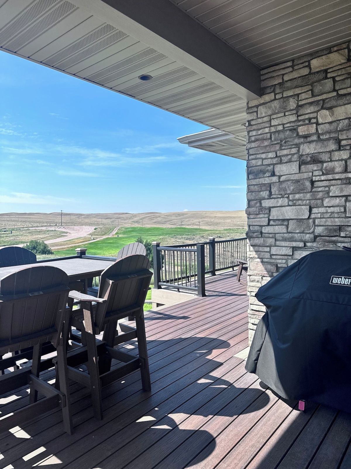 Eine überdachte Terrasse im Freien mit einer Steinmauer, einem Grill und Blick auf eine grüne Landschaft.