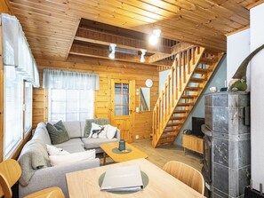 Interior acogedor de una cabaña con escalera de madera, un sofá, una mesa y una chimenea.