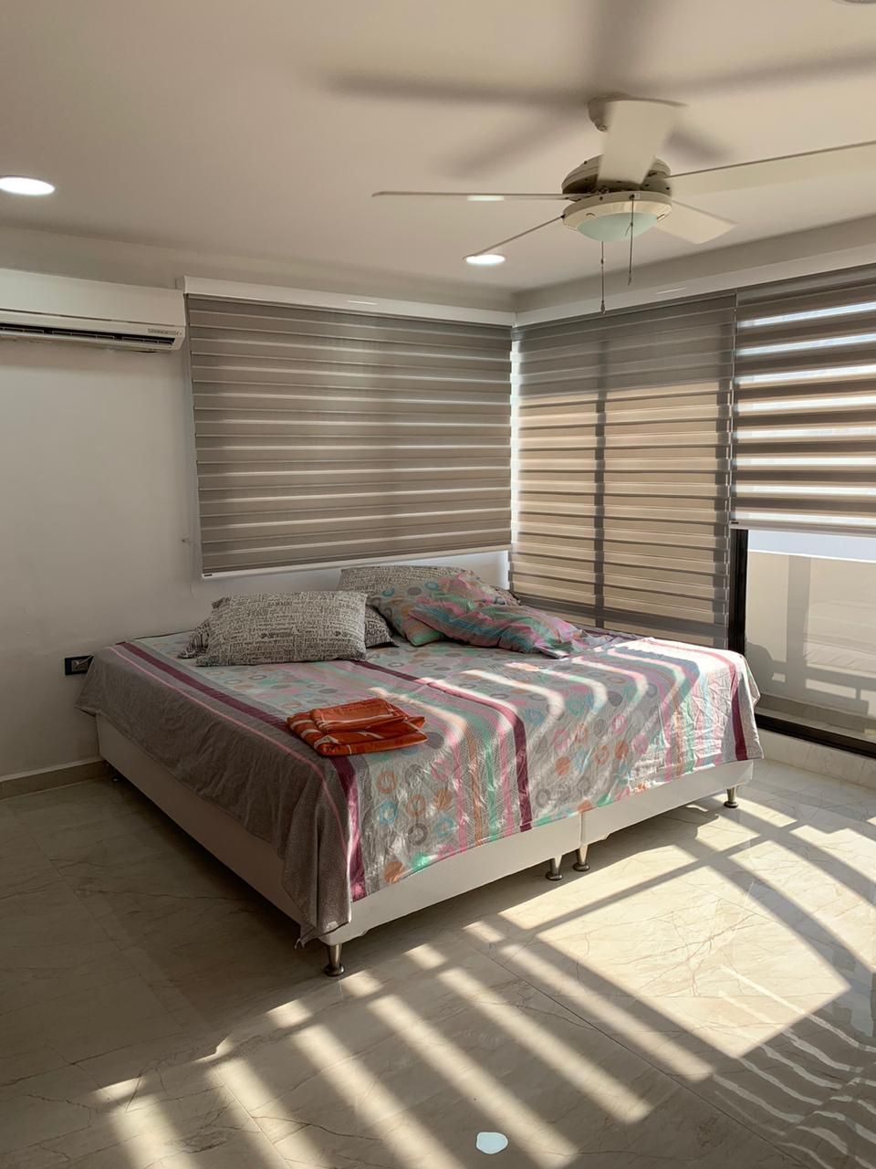 Una camera da letto con un letto, ventilatore a soffitto e ampie finestre con tende.