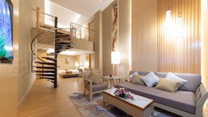 A modern living room with a spiral staircase, a sofa, a coffee table with flowers, and a large painting on the wall. - Glenmarie Hotel & Golf Resort (Shah Alam)