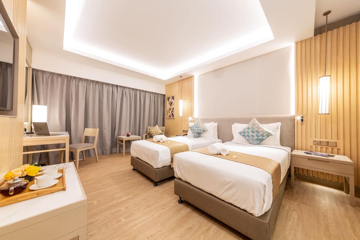 Habitación de hotel con dos camas, un escritorio, una silla, una mesita con una bandeja de desayuno y un ventanal con cortinas.