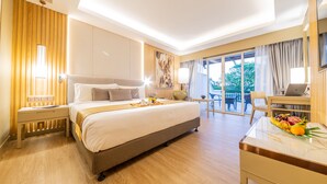 A hotel room with a large bed, a desk with a laptop, a dining table with fruit, and a balcony with a view. - Glenmarie Hotel & Golf Resort (Shah Alam)