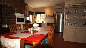 A kitchen with a brick wall, wooden cabinets, and a dining area with a red table and chairs. - Bayside walks and local beach access, in the heart of the Bellarine and wineries (Clifton Springs)