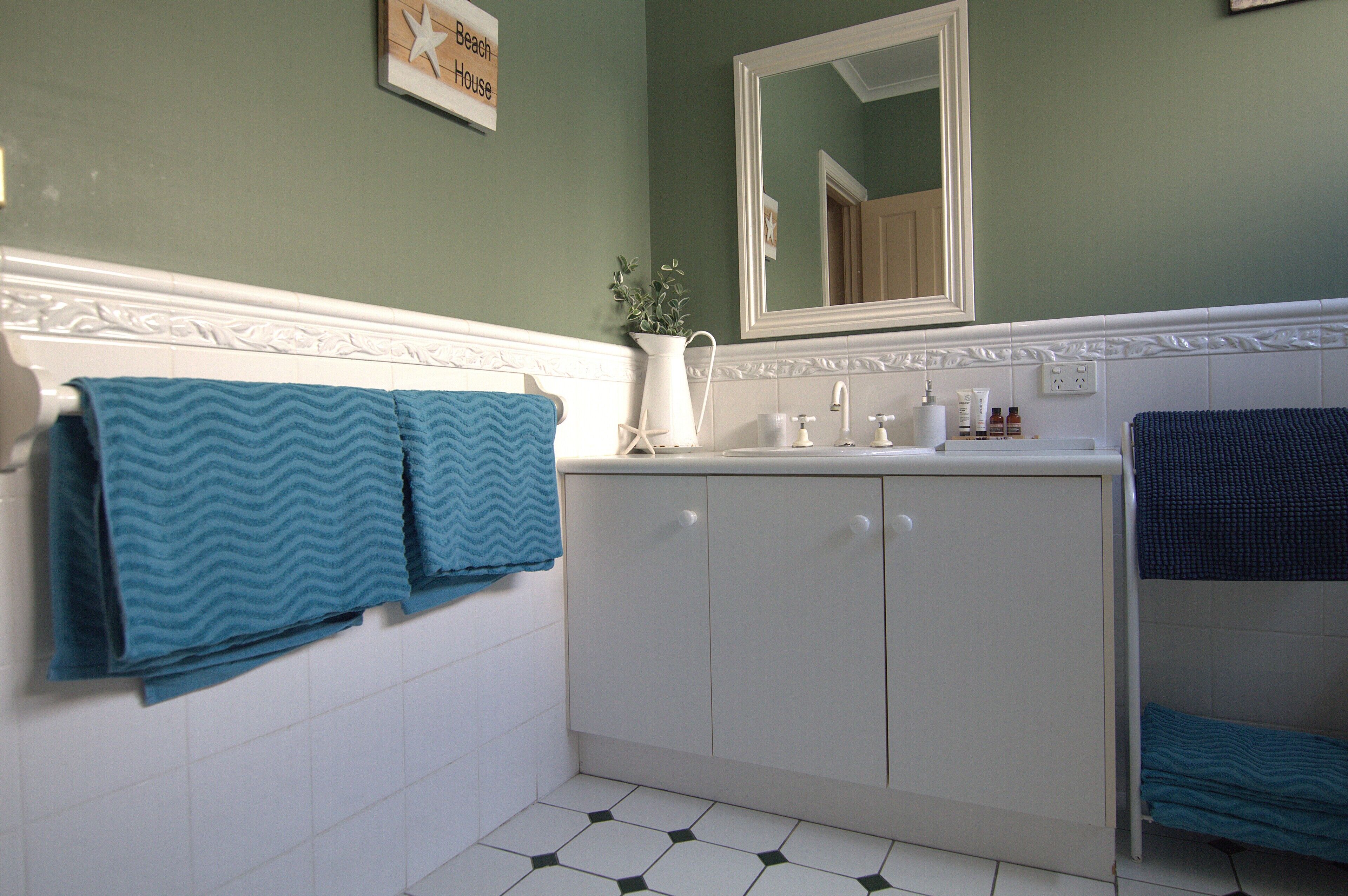 Une salle de bain avec un meuble-lavabo blanc, un miroir et deux serviettes accrochées au mur.