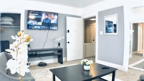 Ein modernes Wohnzimmer mit einem Wand-Fernseher, einem schwarzen Couchtisch und einer weißen Orchideenpflanze.