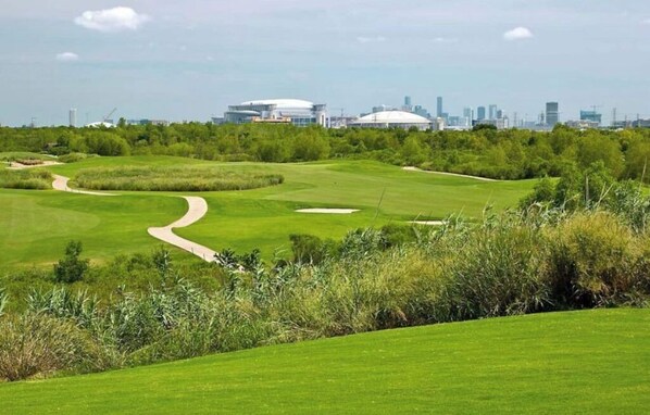 Ein Golfplatz mit einem geschwungenen Weg, üppigem Grün und einer Stadtkulisse im Hintergrund.