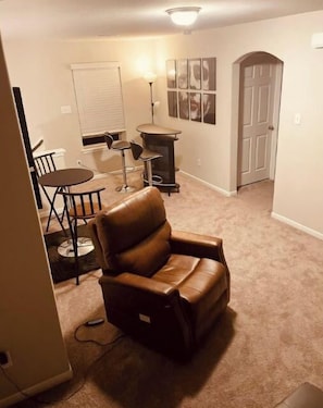 A living room with a brown leather chair, a dining table with chairs, a small round table, and a wall-mounted TV.