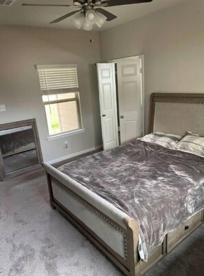 A bedroom with a bed, a ceiling fan, a window with blinds, and a door.