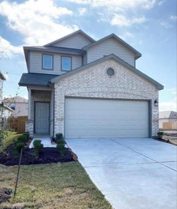 A two-story house with a garage, a front yard with landscaping, and a clear sky.