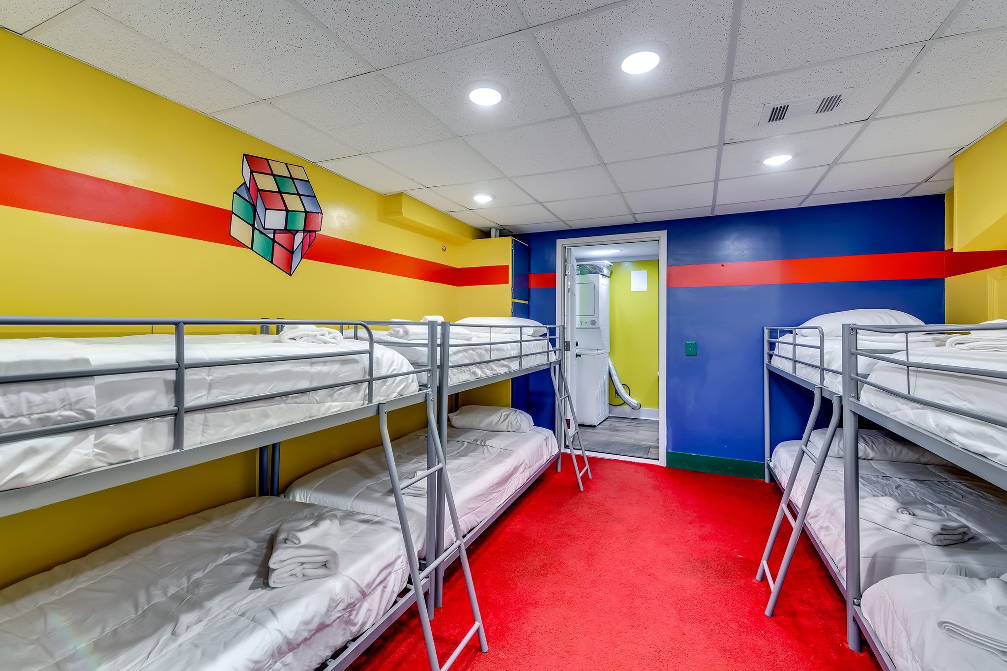 A dormitory room with bunk beds, a red carpet, and a colorful wall design.