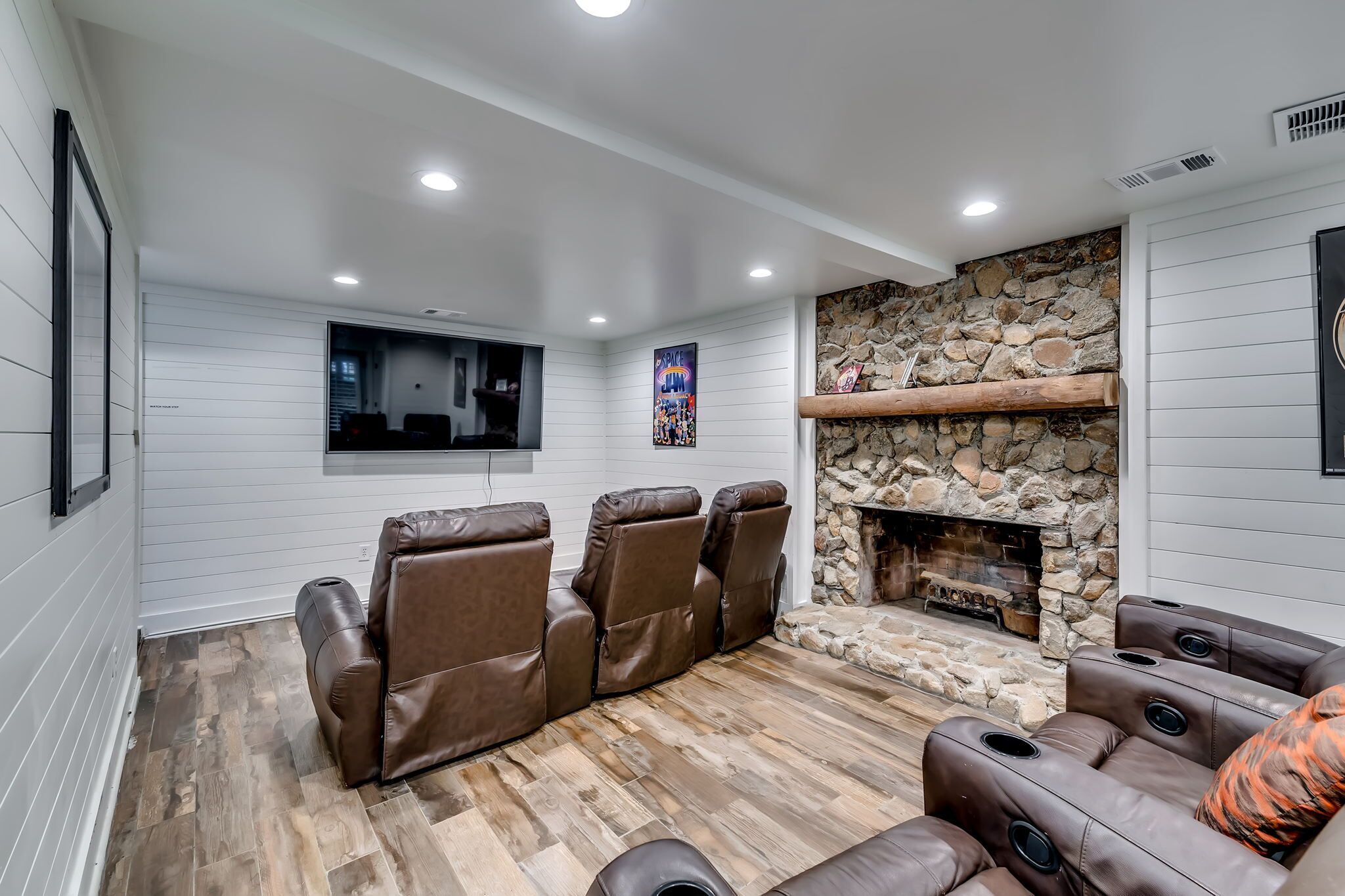 Una sala de estar moderna con chimenea de piedra, sillones de cuero y un televisor montado.