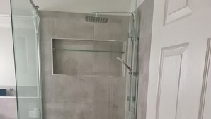Eine begehbare Dusche mit Glastür, gefliesten Wänden und einer kleinen Ablage.