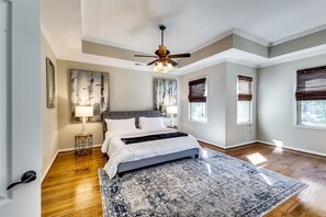 Quarto com cama, ventoinha no teto, tapete e duas janelas com persianas.