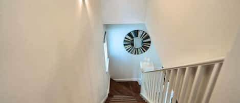 A staircase with a white railing and a wall-mounted clock.