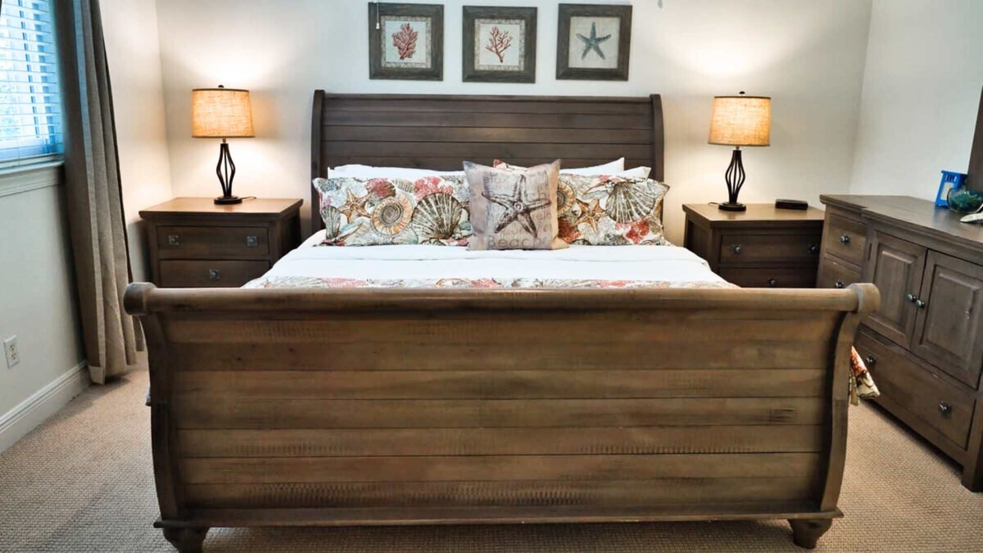A bedroom with a wooden bed, two bedside tables with lamps, a dresser, and three framed pictures on the wall.