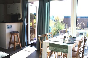 A dining area with a table and chairs, a view of the outdoors, and a sign indicating a beach direction. - Baltic Sea coast, beachfront lodge in Süsel, Lübeck Bay, vacation home (Süsel)