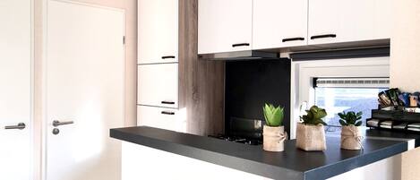 A modern kitchen with white cabinets, a black countertop, and a built-in stove. There are three potted plants on the countertop.