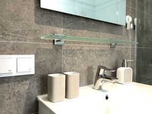 Ein modernes Badezimmer mit Marmorwand, Ablagefläche aus Glas, Waschbecken in Weiß, einem Wasserhahn und zwei beige farbenen Trinkgläsern.