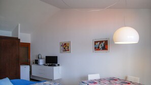 A small, modern room with a bed, a desk with a computer, a microwave, and two paintings on the wall.