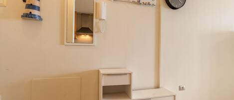 A room with a white bedside table, a mirror, a clock, and a decorative item on the wall.