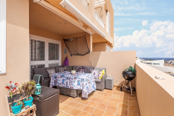 Een balkon met een tafel, stoelen, een grill en planten in potten.
