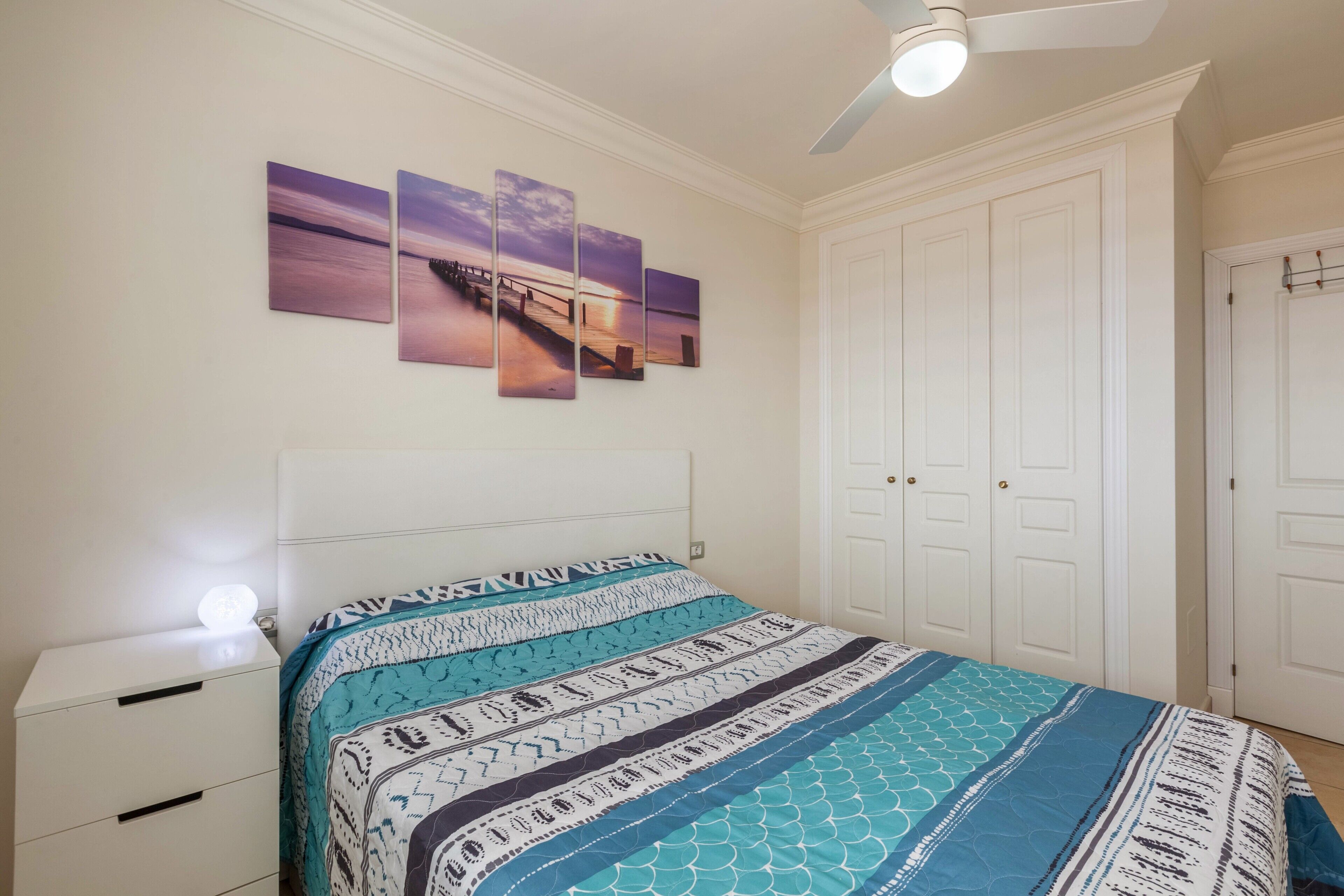 A bedroom with a bed, a nightstand, a ceiling fan, and a set of white doors.