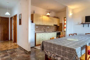 A kitchen with wooden cabinets, a dining table with a checkered tablecloth, and a TV mounted on the wall.