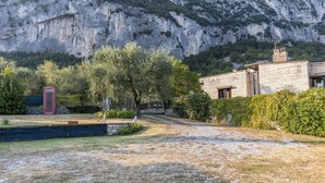 A stone building with a garden, a red telephone booth, and a mountainous backdrop. - Holiday Apartment 'Casa Zanoni' with Lake View, Shared Garden, Balcony & Wi-Fi (Arco)