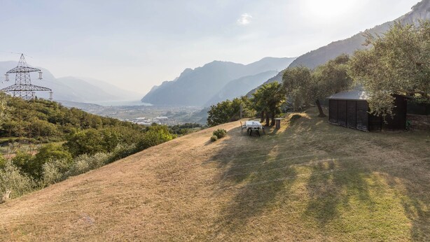 A hilly landscape with a power line tower, a small building, and a distant view of mountains and a valley. - Holiday Apartment 'Casa Zanoni' with Lake View, Shared Garden, Balcony & Wi-Fi (Arco)